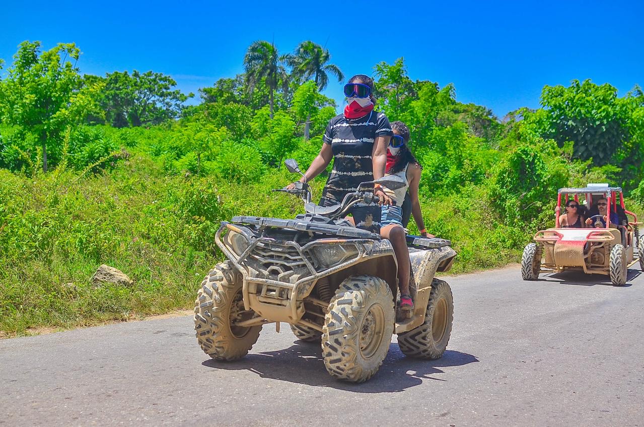 Dos viajeras en cuatrimoto por una carretera entre vegetación, con un buggy detrás